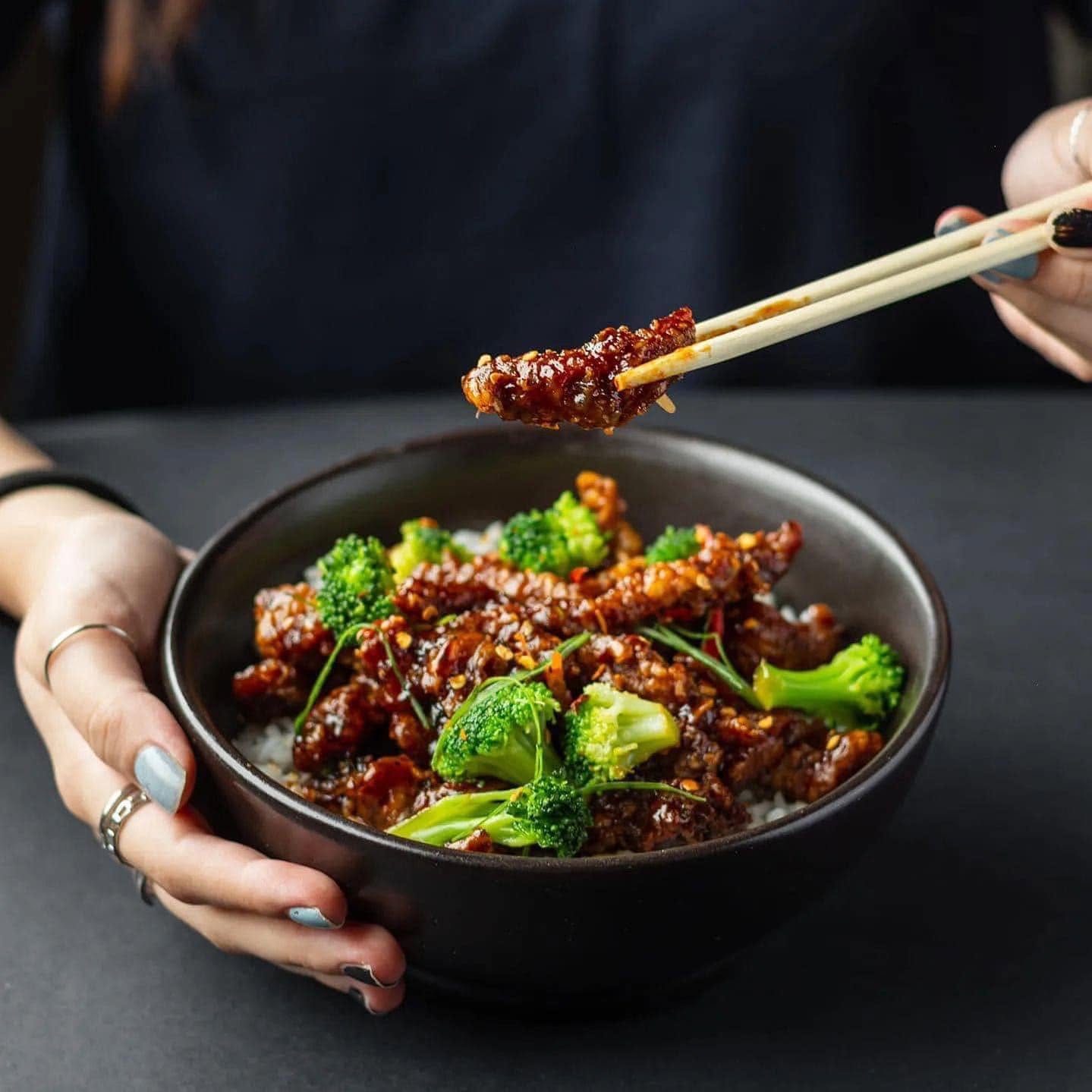 Crispy beef with broccoli over rice, lifted with chopsticks